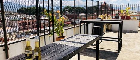 A rooftop terrace with a wooden table, two bottles of beer, and potted plants.