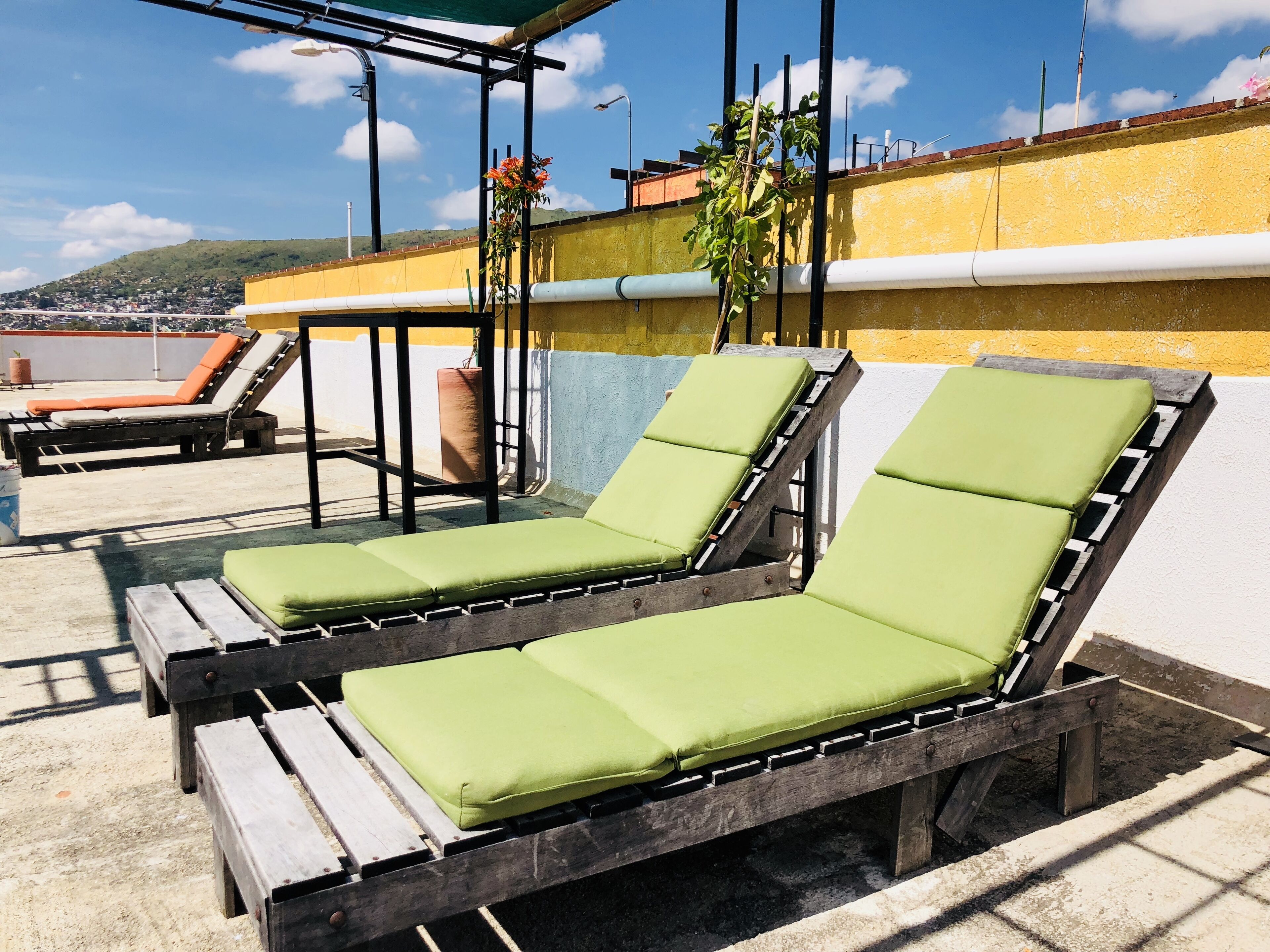Two wooden lounge chairs with green cushions on a rooftop terrace.