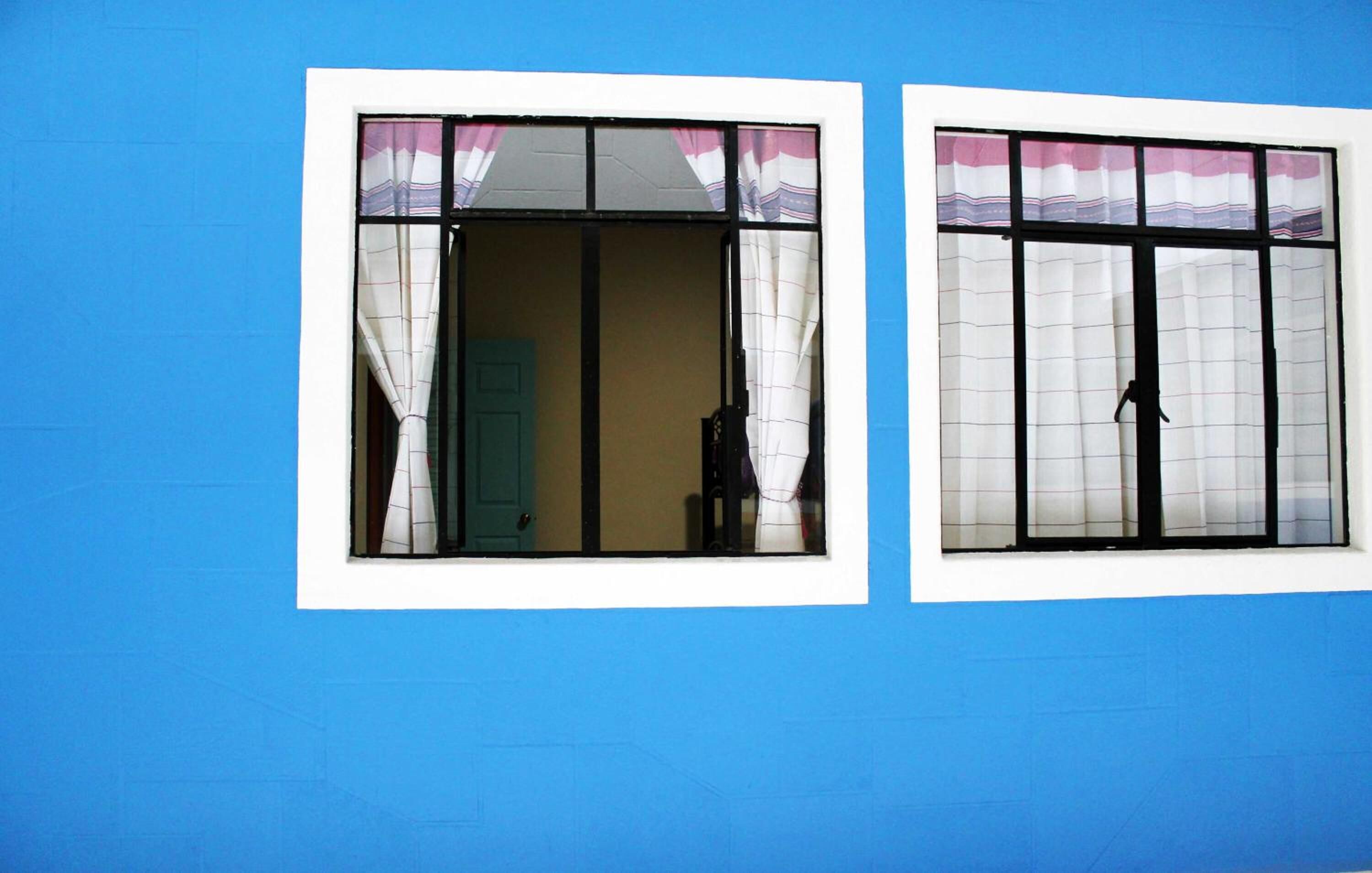 Two windows with curtains, a blue wall, and a door.