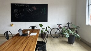 Uma sala de conferências com mesa de madeira, cadeiras, um laptop, um quadro-negro com a inscrição 'CO-WORKING' e uma bicicleta.