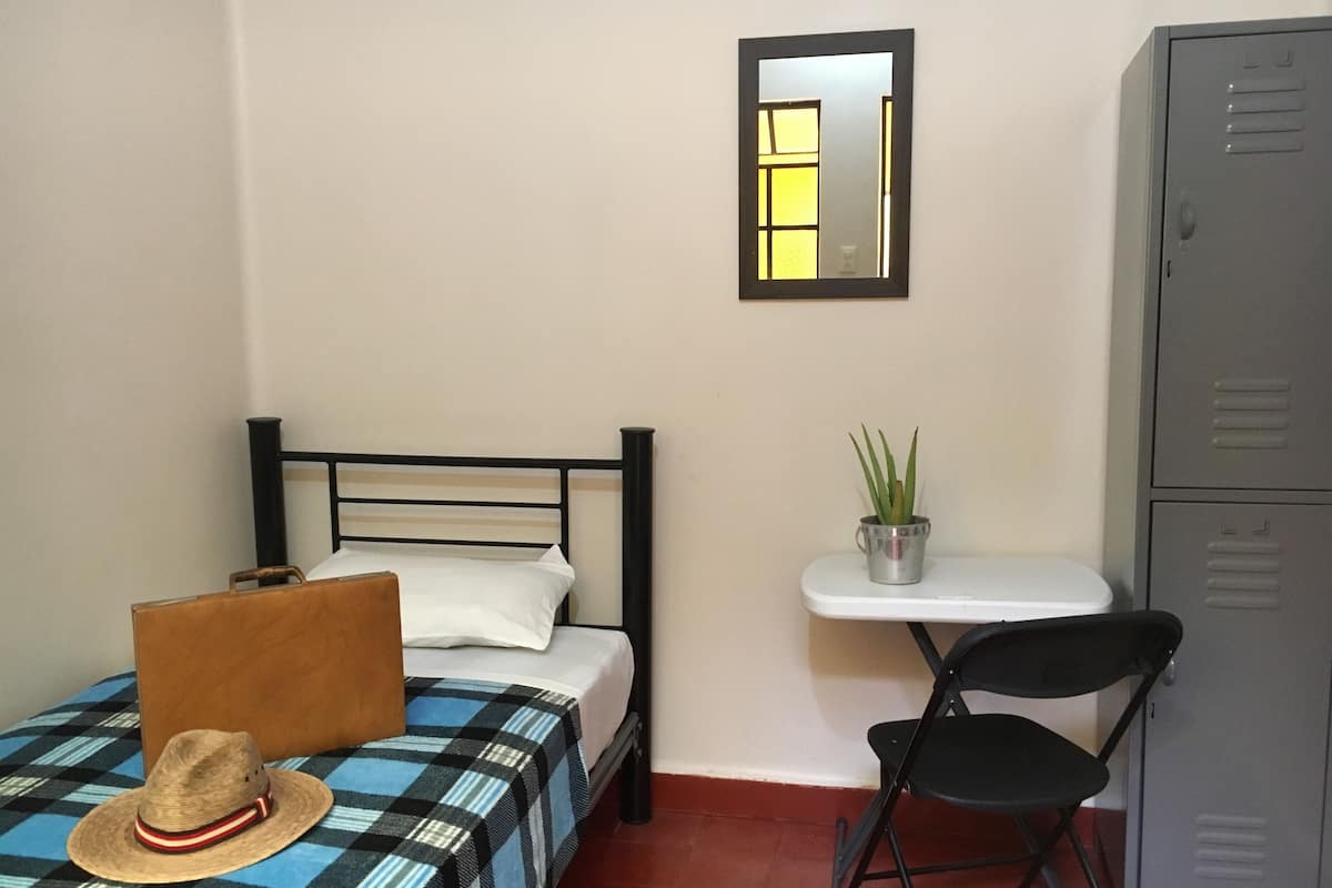 Une petite chambre à coucher, bien rangée, avec un lit, une chaise, un bureau et une armoire.