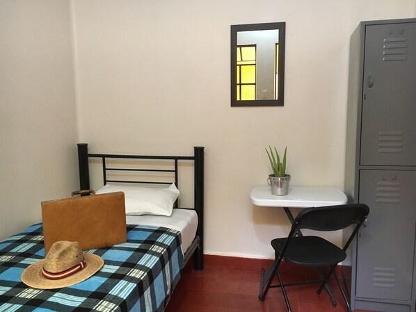 Un dormitorio pequeño y ordenado con cama, una silla, escritorio y armario.