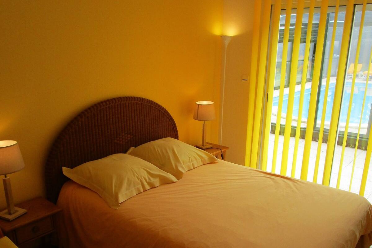 Ein Bett mit Kopfteil, zwei Nachttischlampen und einem Fenster mit Jalousien.