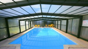 An indoor swimming pool with clear glass walls, yellow lounge chairs, and a tiled floor. - Locatlantique (Aytre)