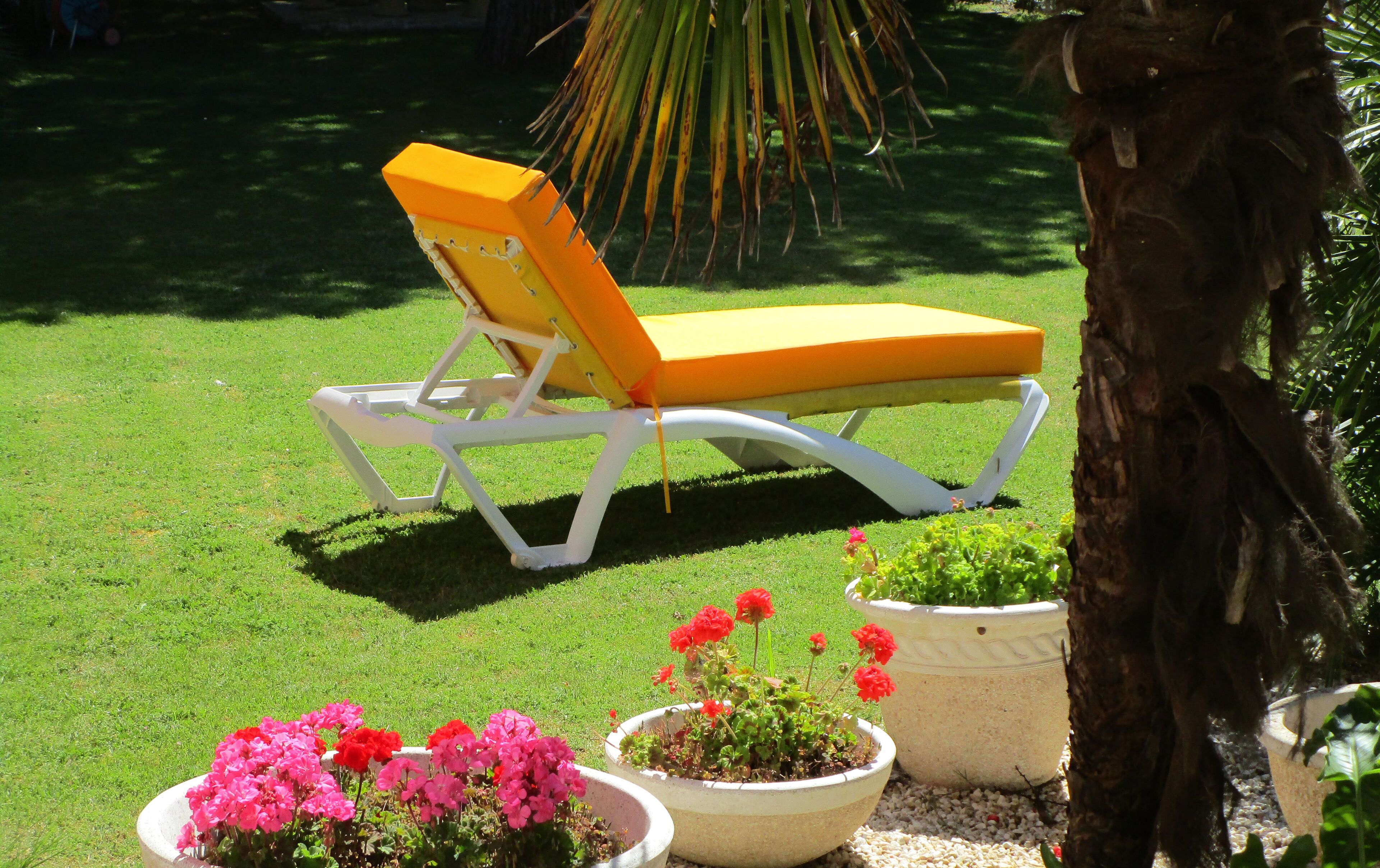 A white and yellow lounge chair on a grassy lawn with potted plants nearby.