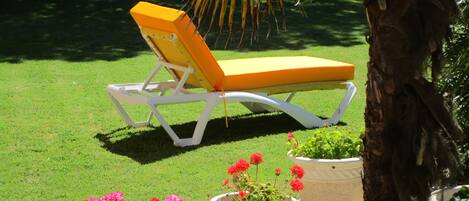 A white and yellow lounge chair on a grassy lawn with potted plants nearby.