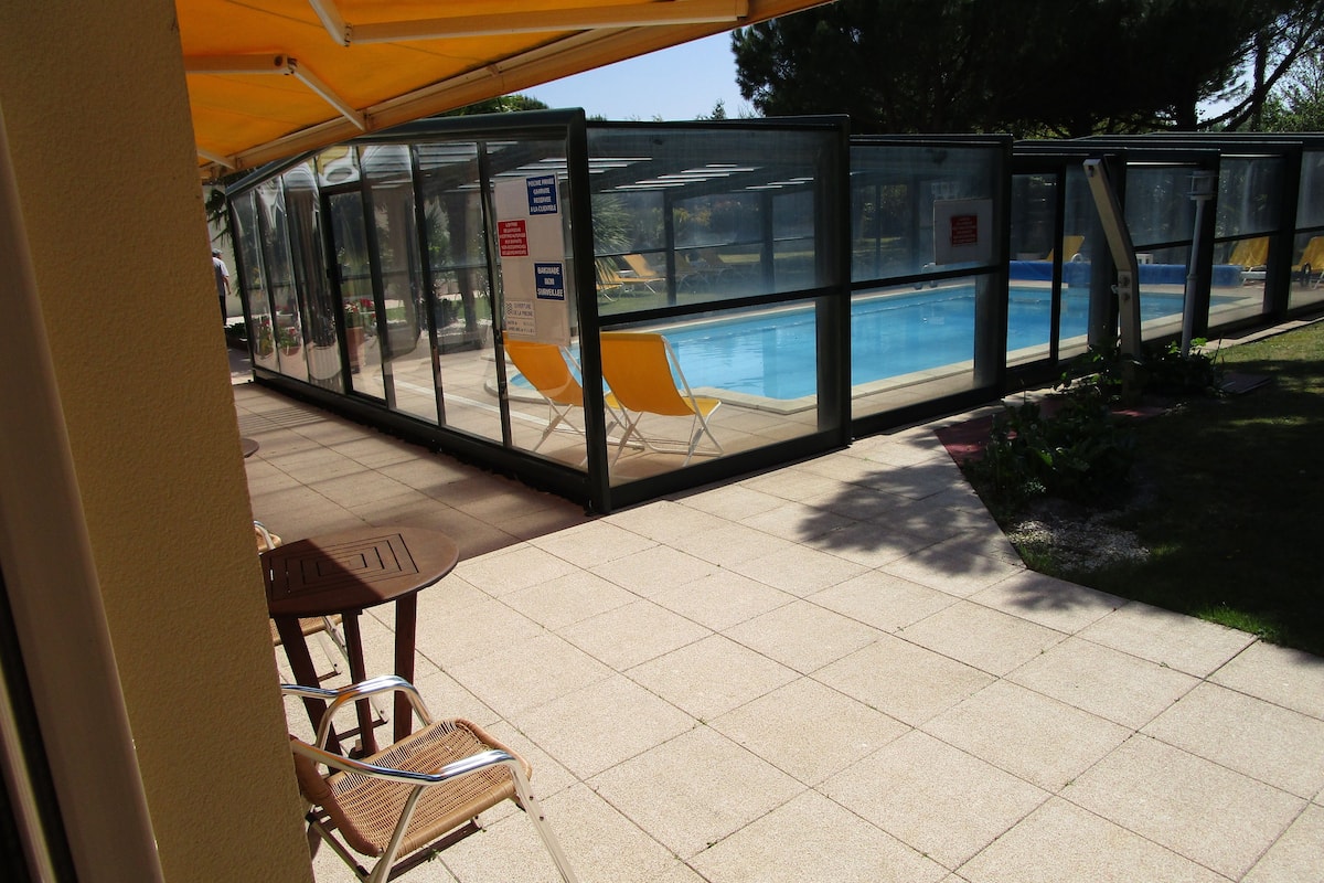 Ein überdachter Außenbereich mit Pool, Glasumrandung und Sitzgelegenheiten.