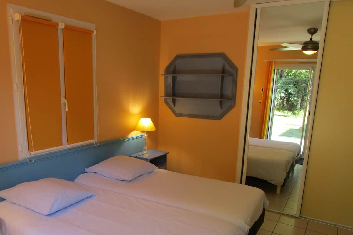 Ein Hotelzimmer mit zwei Betten, einem Nachttisch mit Lampe, einem Deckenventilator und einem großen Spiegel.
