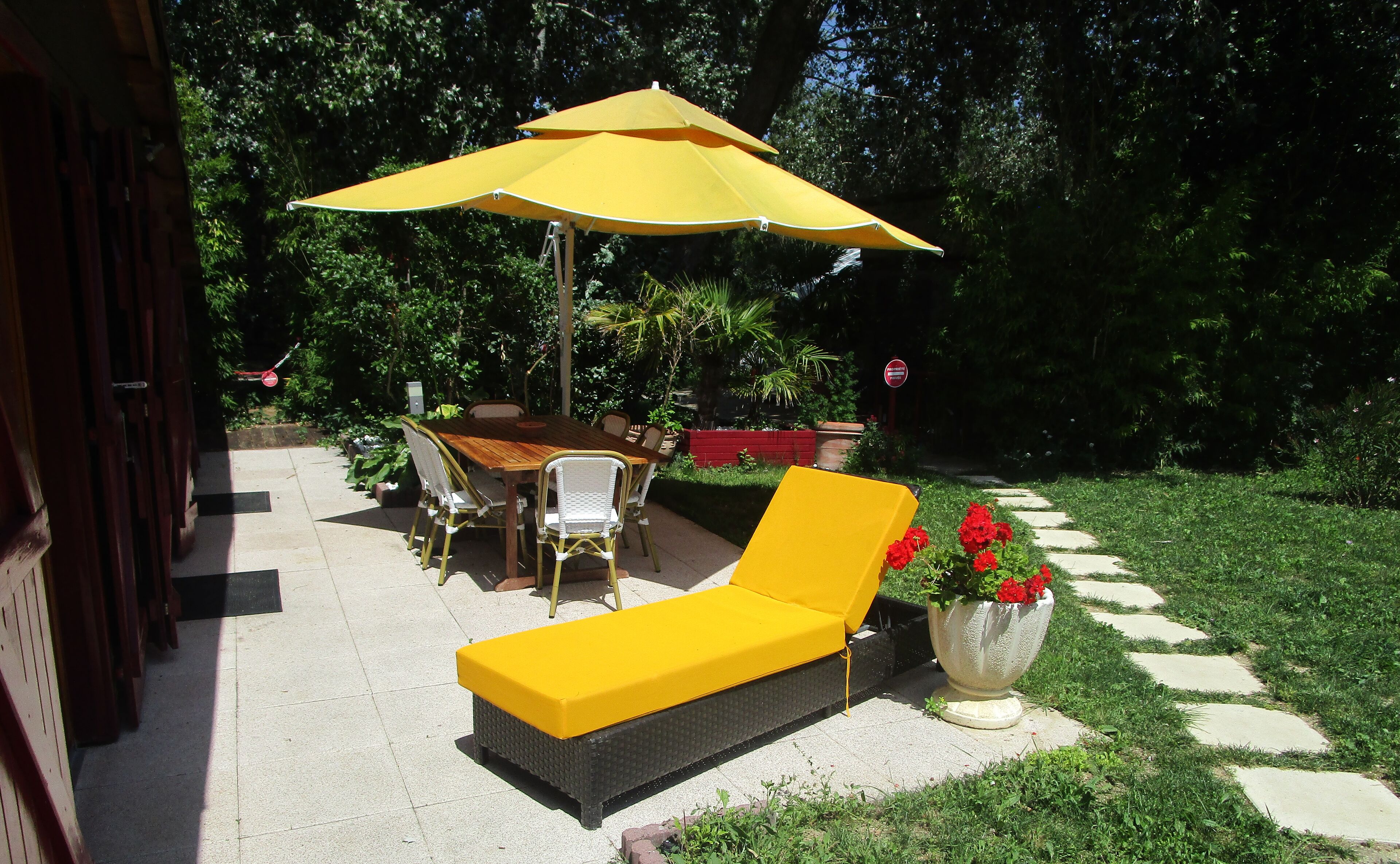 An outdoor patio with a wooden table, yellow lounge chairs, and a large yellow umbrella.
