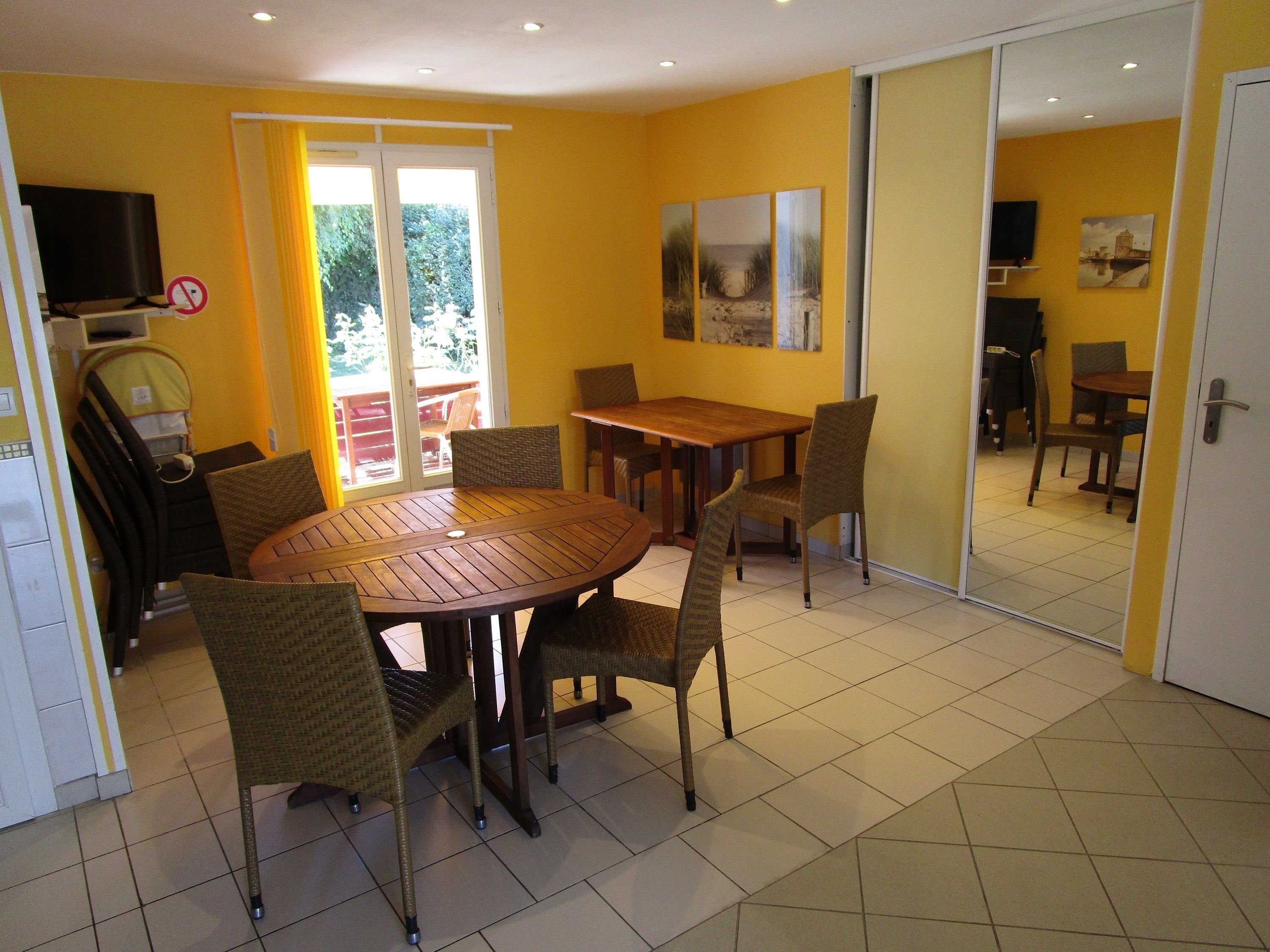 A dining area with a round wooden table and wicker chairs, a television, and a sliding glass door to a balcony.