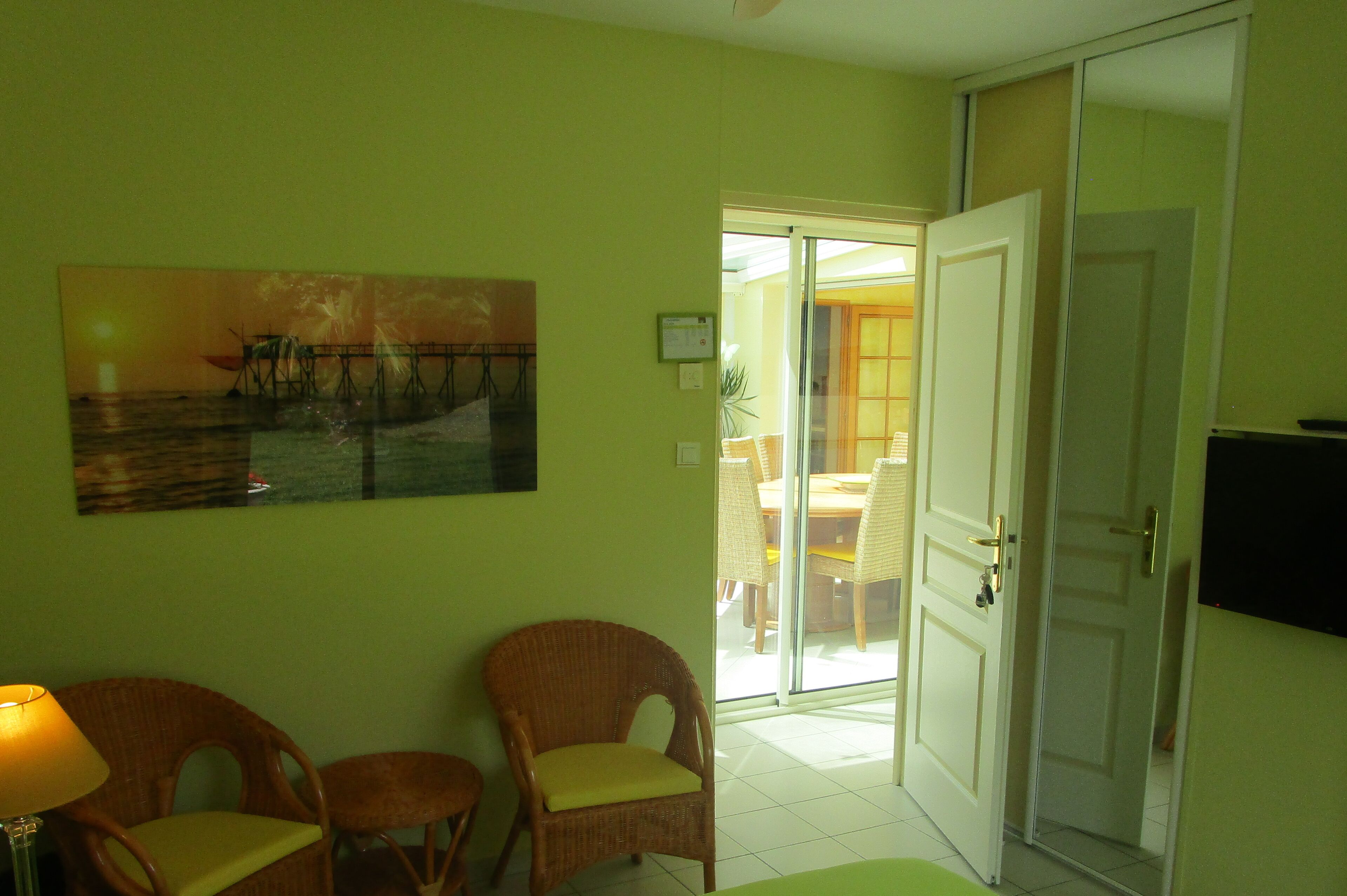 Ein Zimmer mit einem Gemälde von einem Steg, Korbstühlen, einer geschlossenen Tür und einem Fernseher.