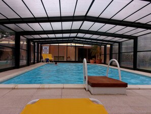 An indoor swimming pool with clear water, a wooden deck, and a yellow lounge chair. - Locatlantique (Aytre)