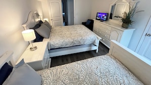 Une chambre à coucher comprenant un lit, une table de chevet, une lampe, une commode, un téléviseur et un ventilateur de plafond.