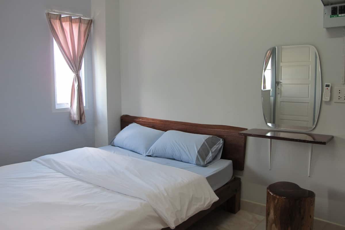 A bedroom with a bed, a bedside table, a mirror, and a window with curtains.