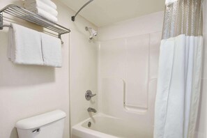 Une salle de bain avec une baignoire blanche, une pomme de douche, un porte-serviettes avec des serviettes pliées et des toilettes.