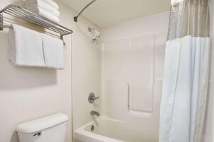 Un baño con una bañera blanca, una ducha, un tendedero de toallas con toallas dobladas y un inodoro.