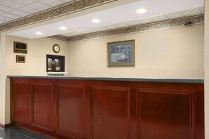 A reception area with a wooden reception desk, a clock, and framed artwork on the wall. - Days Inn by Wyndham Lexington (Lexington)