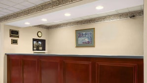 A reception area with a wooden reception desk, a clock, and framed artwork on the wall. - Days Inn by Wyndham Lexington (Lexington)