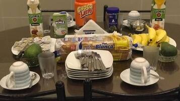A dining table set with plates, cutlery, a loaf of bread, bananas, and various condiments.
