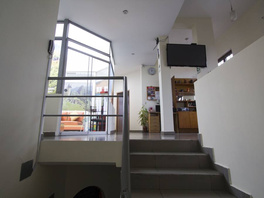 Uma escada leva a uma área de estar com uma janela ampla, uma TV de tela plana fixada na parede e uma cozinha ao fundo.