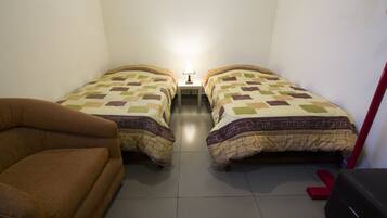 Een kamer met twee bedden, een nachtkastje met lamp, een bruine bank en een rode bank.