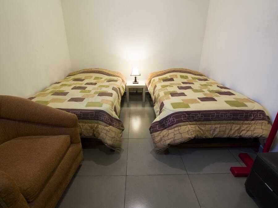 Een kamer met twee bedden, een nachtkastje met lamp, een bruine bank en een rode bank.