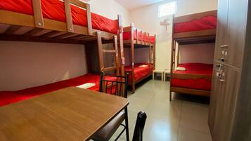 A dormitory room with bunk beds, a wooden table, and a chair.
