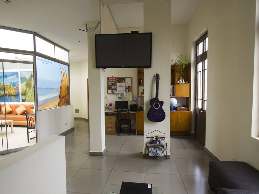 Un salón amplio con un gran ventanal, un televisor de pantalla plana, una guitarra y un escritorio con una computadora.