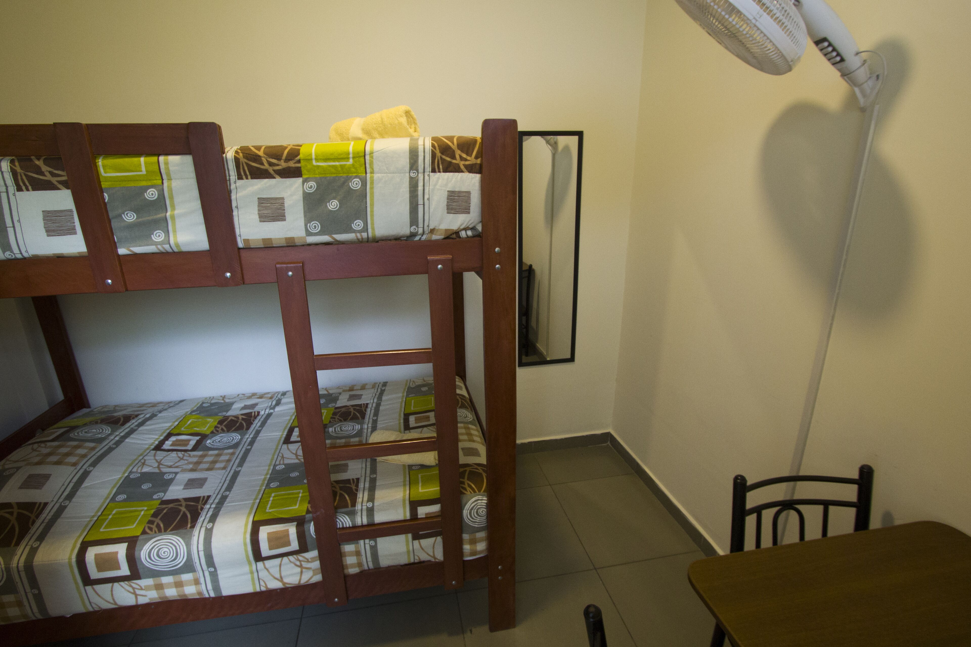 Una litera con ropa de cama estampada, un escritorio y un ventilador de pie.