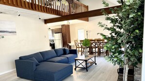 A modern living room with a sectional sofa, a coffee table, and a dining area with wooden chairs and a table. - FREE Amenity Passes Spacious Sauna Large Deck Firepit (Lehman township)