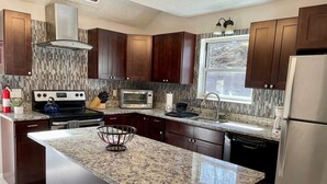 A modern kitchen with dark wood cabinets, a granite countertop, a stainless steel refrigerator, a built-in oven, a microwave, and a gas stove. - FREE Amenity Passes Spacious Sauna Large Deck Firepit (Lehman township)
