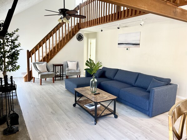 A living room with a blue sofa, a wooden coffee table, and a staircase with wooden railings. - FREE Amenity Passes Spacious Sauna Large Deck Firepit (Lehman township)