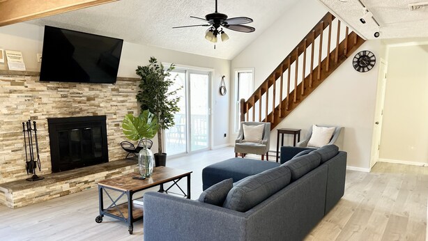 A spacious living room with a stone fireplace, a large gray sofa, a wooden ceiling, and a staircase. - FREE Amenity Passes Spacious Sauna Large Deck Firepit (Lehman township)