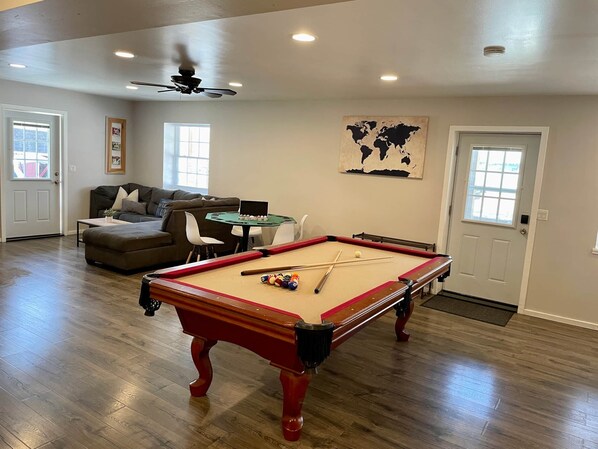 Un salon comprenant une table de billard, un canapé, un ventilateur de plafond et une carte du monde accrochée au mur.