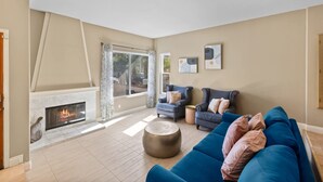 Een woonkamer met een open haard, een blauwe bank en een groot raam.