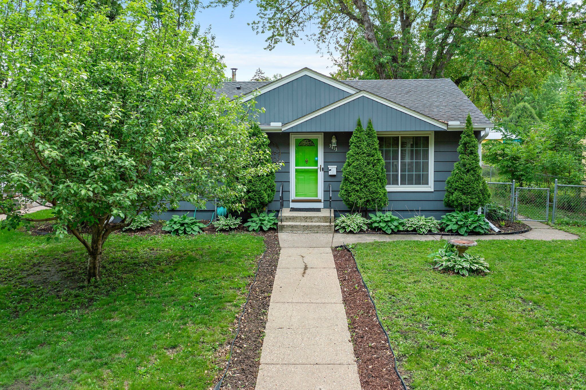 A house with a green front door, a small front porch, and a well-maintained lawn.