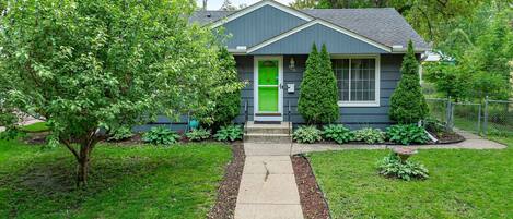 A house with a green front door, a small front porch, and a well-maintained lawn.