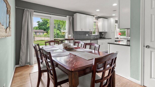 A modern kitchen with white cabinets, a dining area with a wooden table and chairs, and a view of the outdoors. - 10 BEDS in 4 BR! Quiet comforts in the city. (Minneapolis)