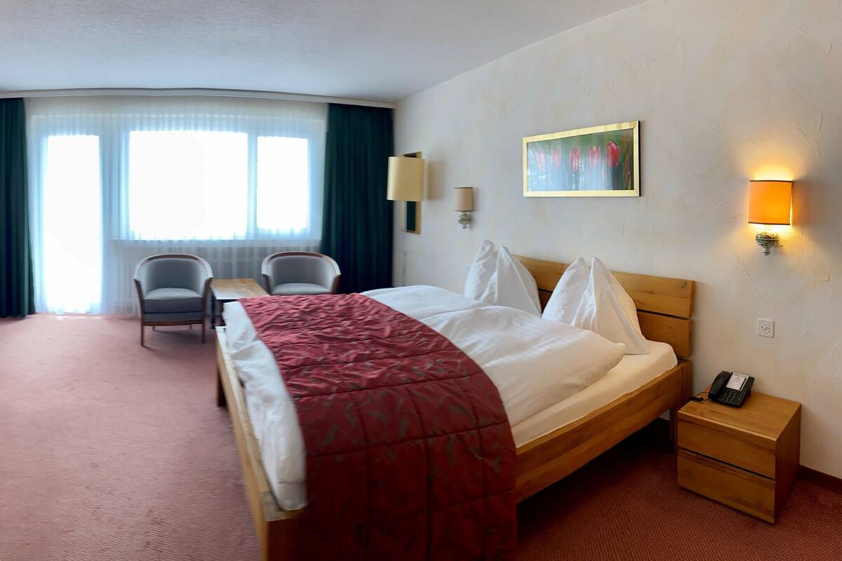 Una habitación de hotel con cama, escritorio, silla, televisor y un cuadro.