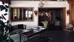 Una habitación con techo de madera, candelabro, ventana grande con vistas, zona de bar y área de descanso con una mesa y libros.