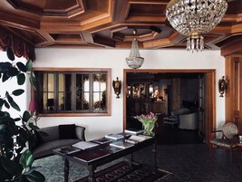 A room with a wooden ceiling, a chandelier, a large window with a view, a bar area, and a seating area with a table and books.