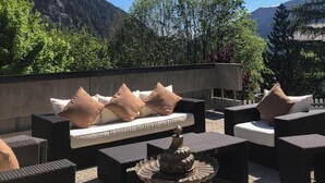 Un área de estar al aire libre con mobiliario de mimbre y cojines, con vistas a un paisaje montañoso.