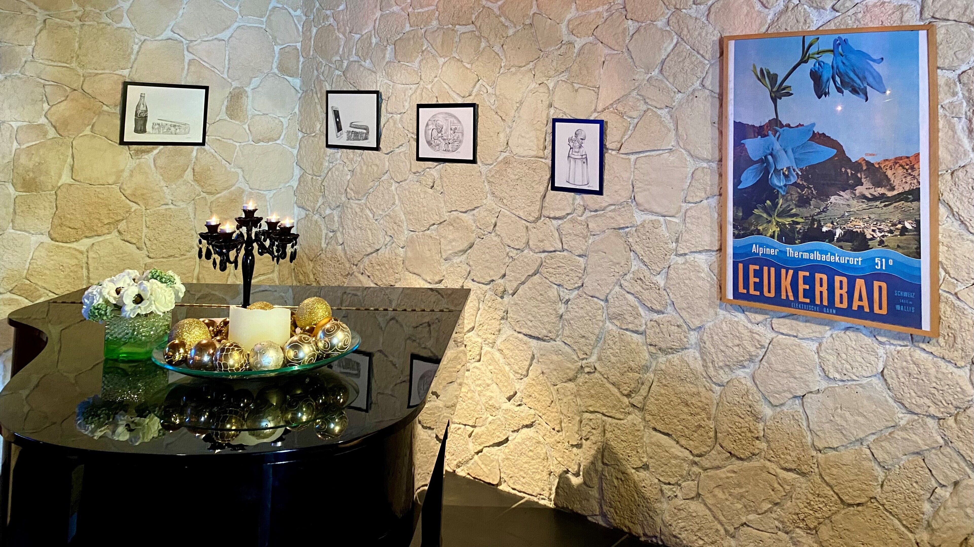 A table with a candle and decorative items, a wall with framed pictures, and a poster of Leukerbad.