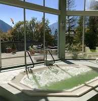 A hot tub with a view of trees and mountains through large windows.
