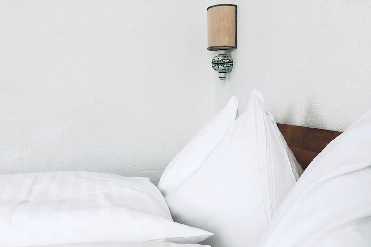 Una cama bien hecha con sábanas blancas y cabecera de madera.