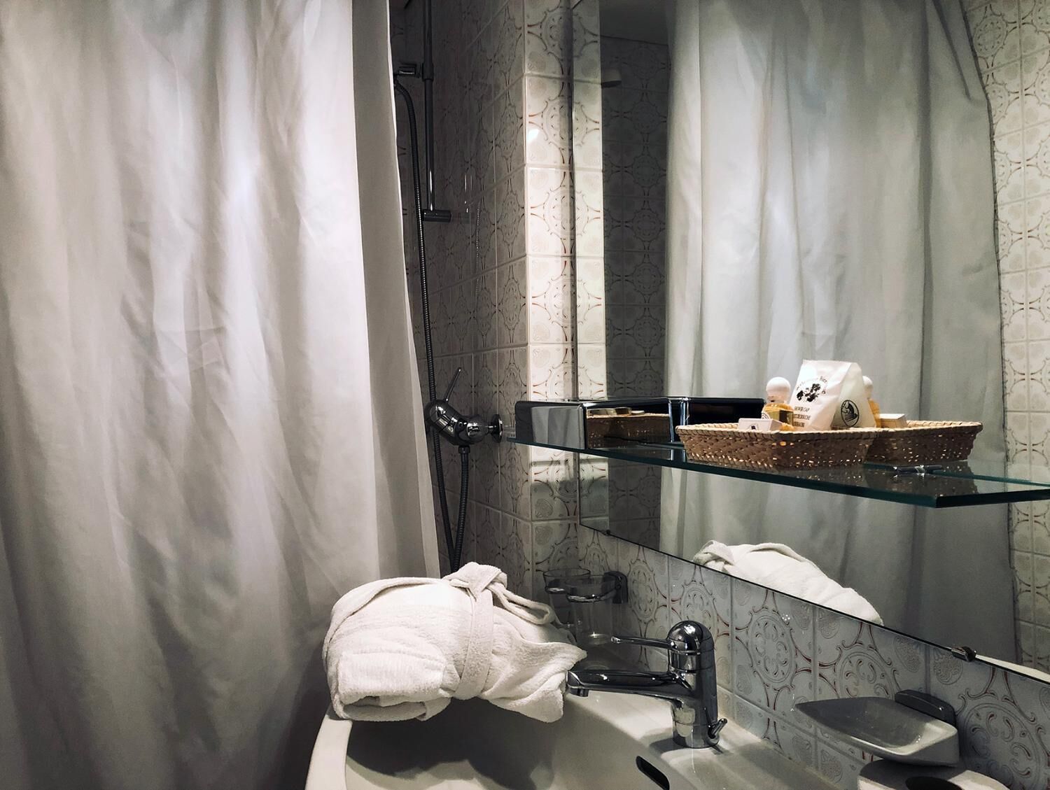 A modern bathroom with a glass shelf holding toiletries, a white towel, and a shower area with a glass door.