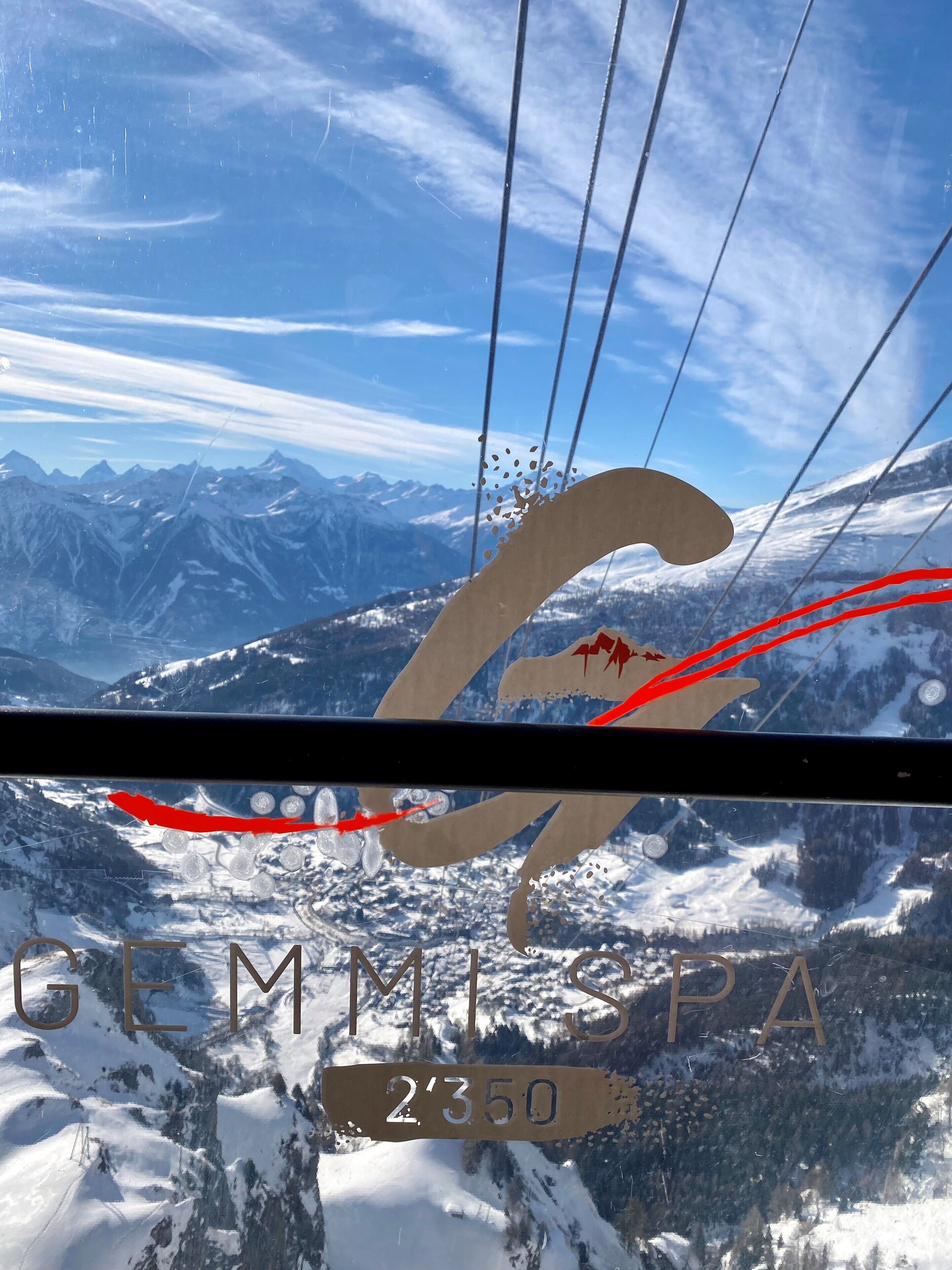 Un teleférico con un logotipo y el texto "GEMMIPA 2350" frente a un paisaje montañoso nevado.
