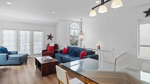 En moderne stue med et glas sofabord, to sofaer og en rød lænestol. Der er en trappe med gelænder og en stjerne dekoration på væggen.