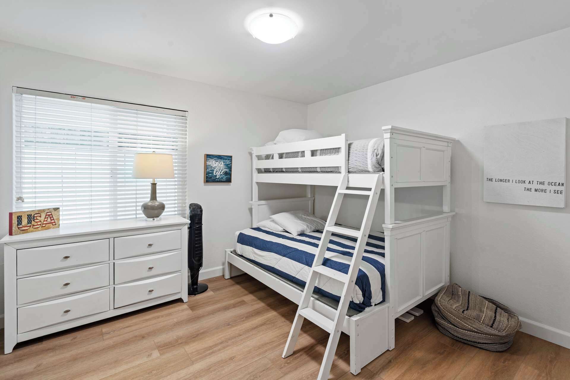 A bunk bed room with a desk, drawers, a lamp, a fan, and a rug.
