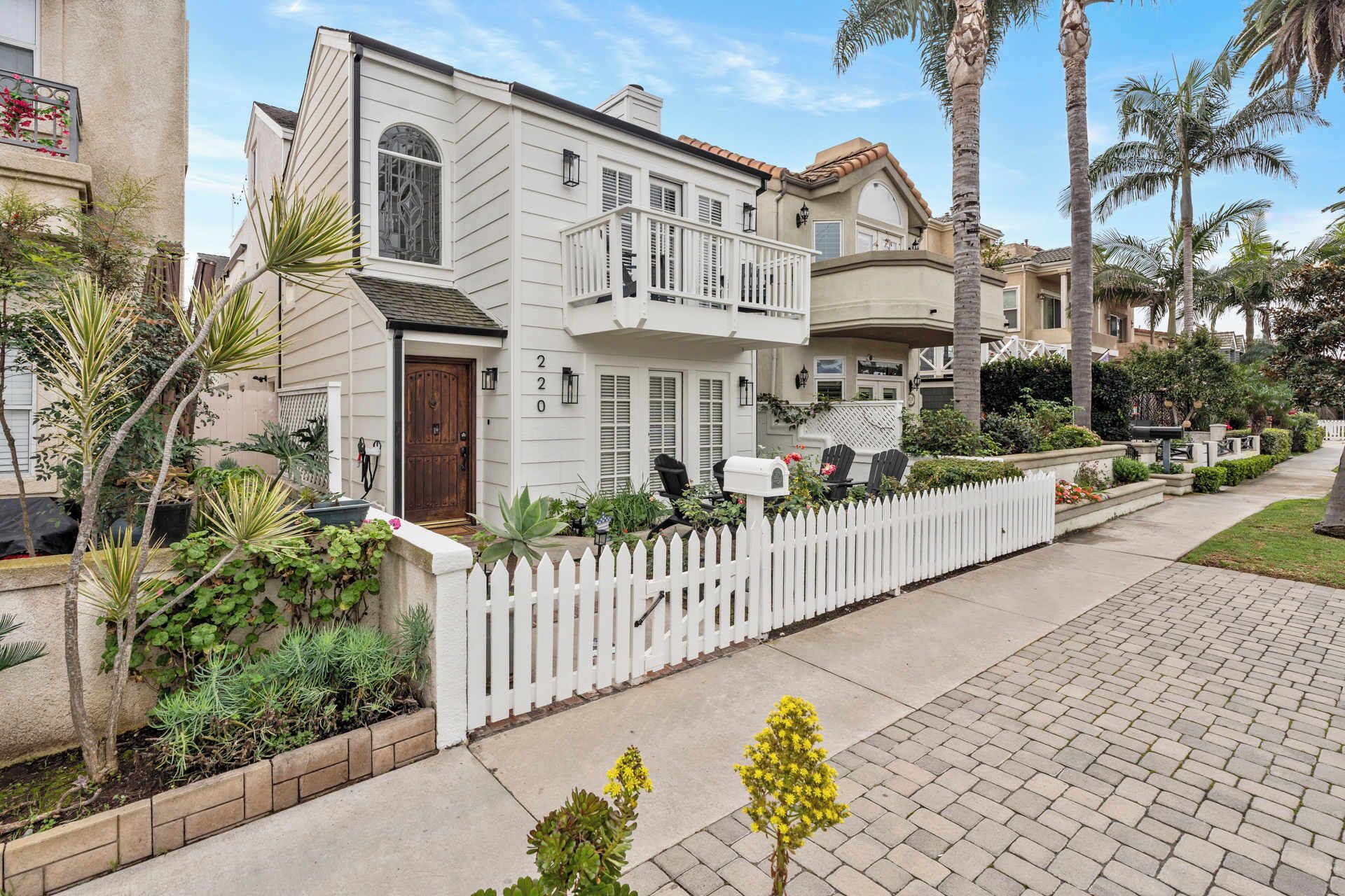 Une maison à deux étages, à l’extérieur blanc, avec un porche à l’avant et une clôture en bois peinte en blanc.